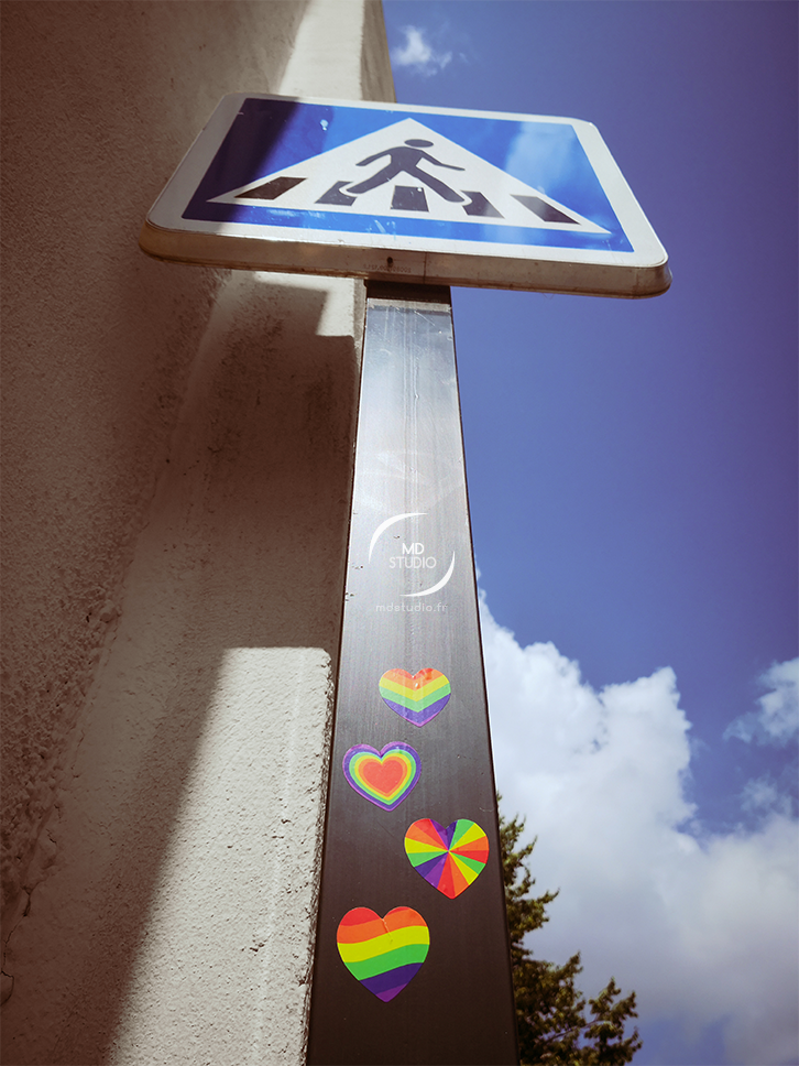 photographie d'un panneau de signalisation et drapeau arc-en-ciel en forme de coeur