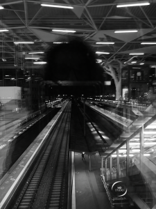 horizon nocturne, photographie depuis la passerelle, gare illuminée. Le rail photographié quitte l'obscurité, révélée par l'ombre sur la vitre